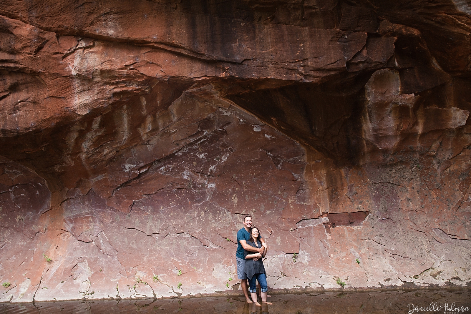 Couple embracing against a red, creek, canyon wall